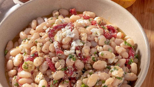 Weißer Bohnensalat mit Feta, roten Paprikastreifen und Zwiebeln in einer Schüssel.