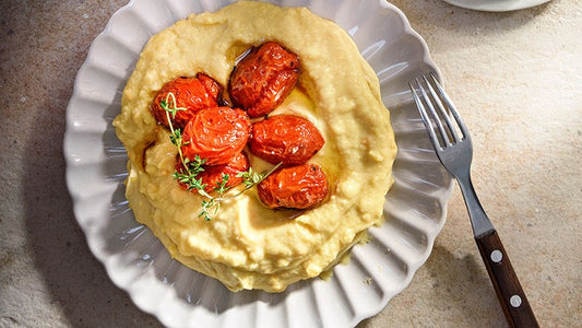 Cremige gelbe Fava mit gebackenen Kirschtomaten und Thymian auf einem Teller.