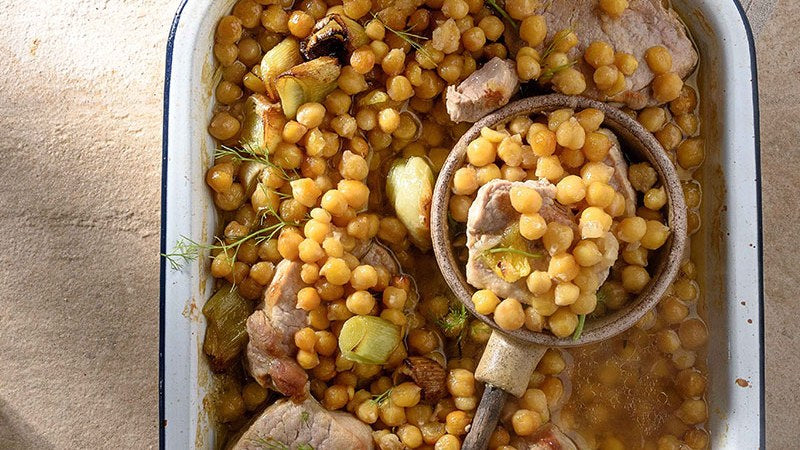 Kichererbsen mit Schweinefleisch, Lauch und Fenchel in einer Auflaufform, mit Löffel.