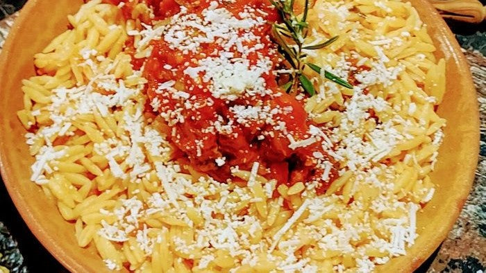 Kritharaki (Teigreis) mit roter Tomatensauce und geriebenem Mizithra auf einem Teller.