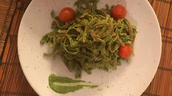 Bandnudeln mit grünem Rucola-Pesto und Kirschtomaten auf einem Teller.