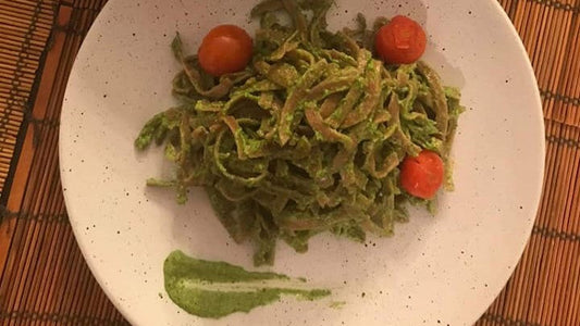 Bandnudeln mit grünem Rucola-Pesto und Kirschtomaten auf einem Teller.