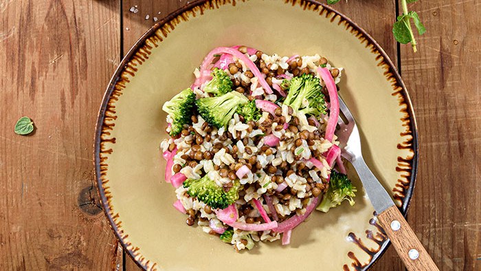 Linsen-Reis-Salat mit Brokkoliröschen und eingelegten roten Zwiebeln auf einem Teller.