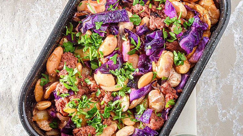 Weiße Riesenbohnen mit Kavourmas und Rotkohl in einer Auflaufform, mit Petersilie.